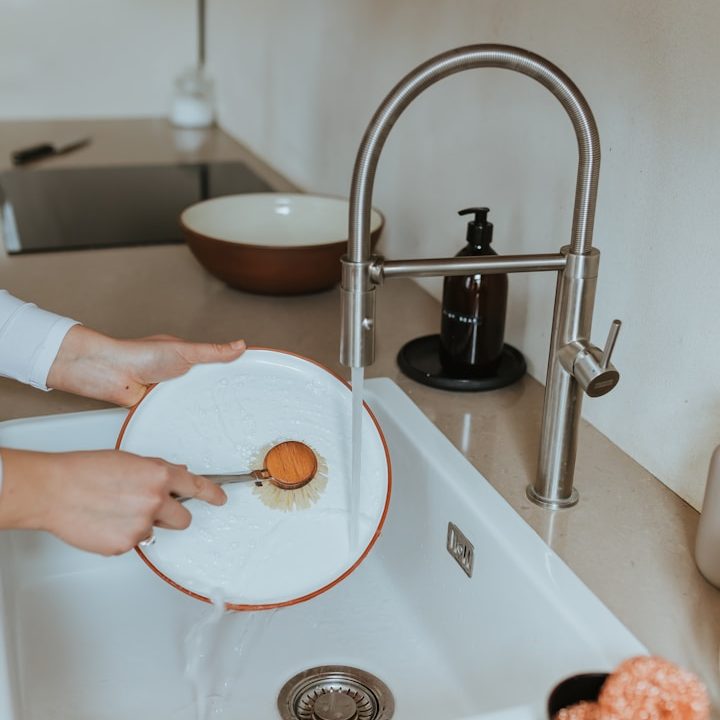 A person washing a plate with a sponge under a kitchen tap.  Hot running water in a mobile kitchen trailer